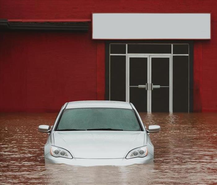 A red building with a car and standing water in the parking lot. 